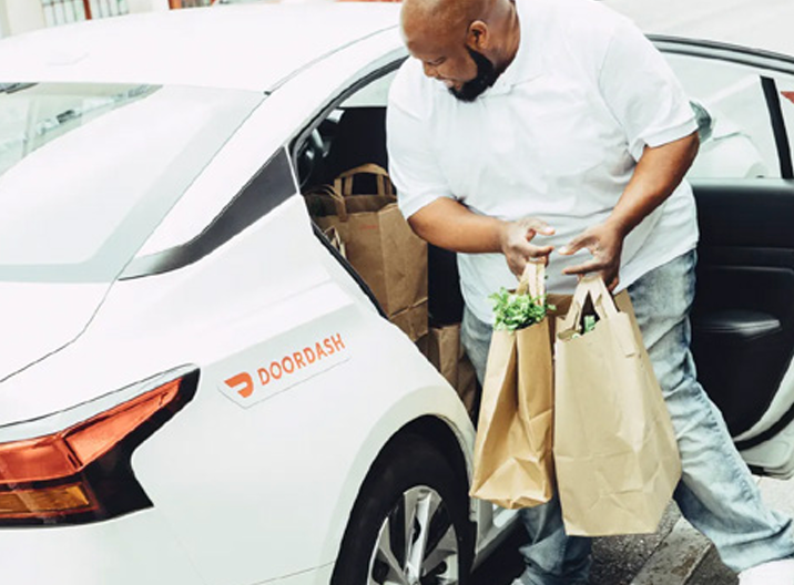 A dasher grabbing paper grocery bags from the backseat of their car