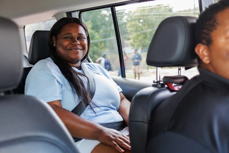A young woman sitting in the back of a car with a driver up front