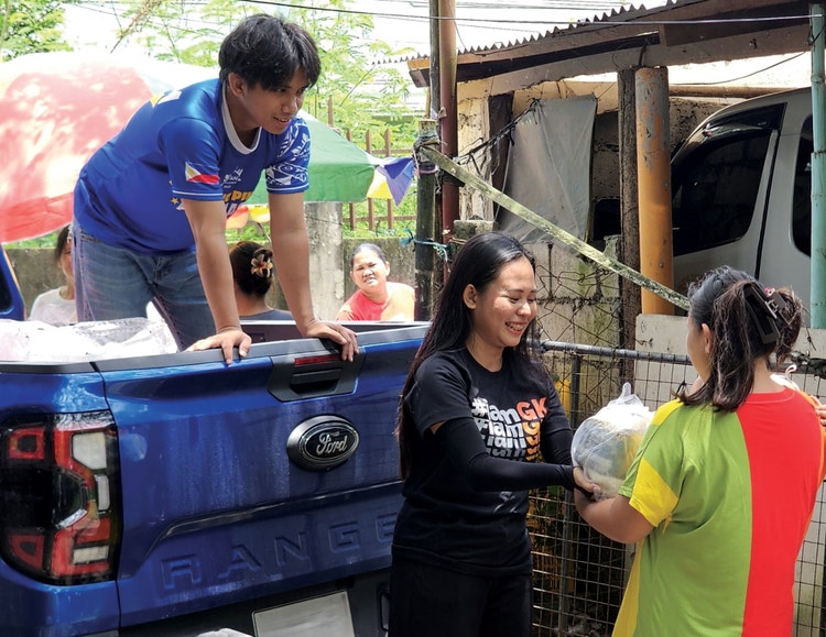 Young man in the back of a pickup truck handing supplies to women on the ground