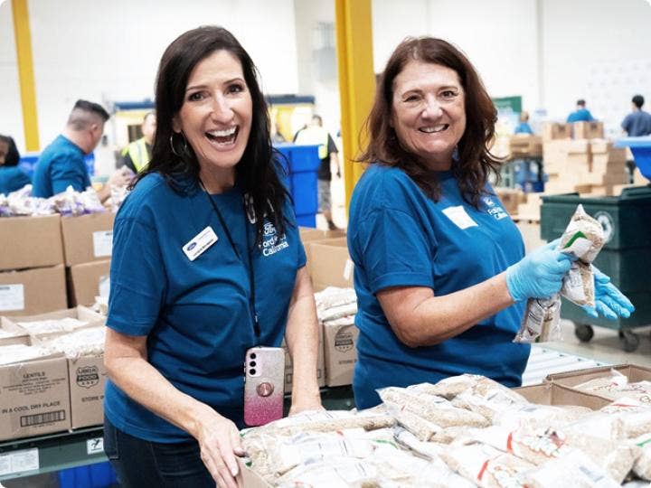 Women in blue shirts holding a box of food AI-generated content may be incorrect.
