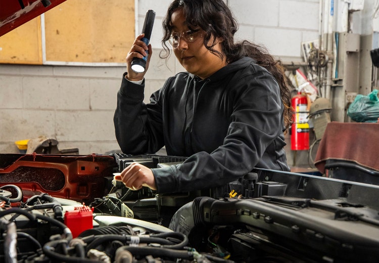 Young woman with a flashlight looking under the hood at the shop