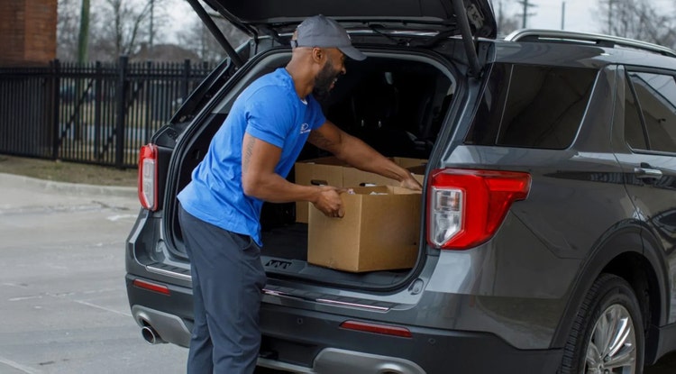 Blue shirt Ford volunteer placing a box of food in someones trunk
